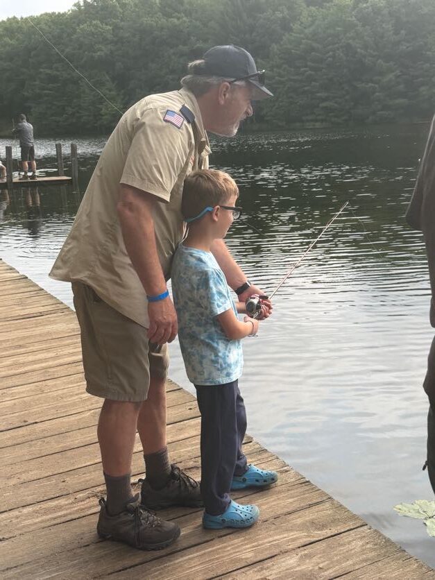 Adult leader helping a Scout fish from the dock