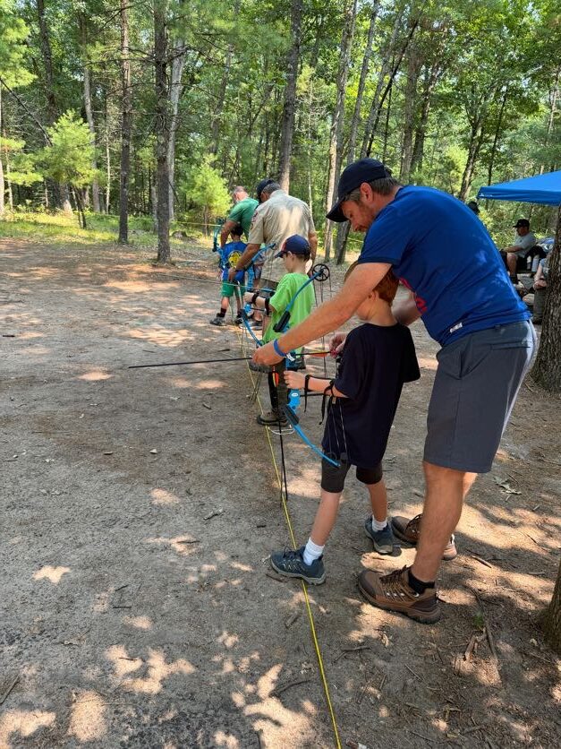 Adult volunteer helping a Scout practice archery