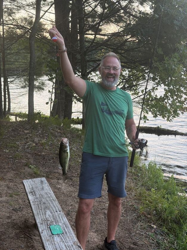 Adult volunteer holding a freshly caught fish near the lake